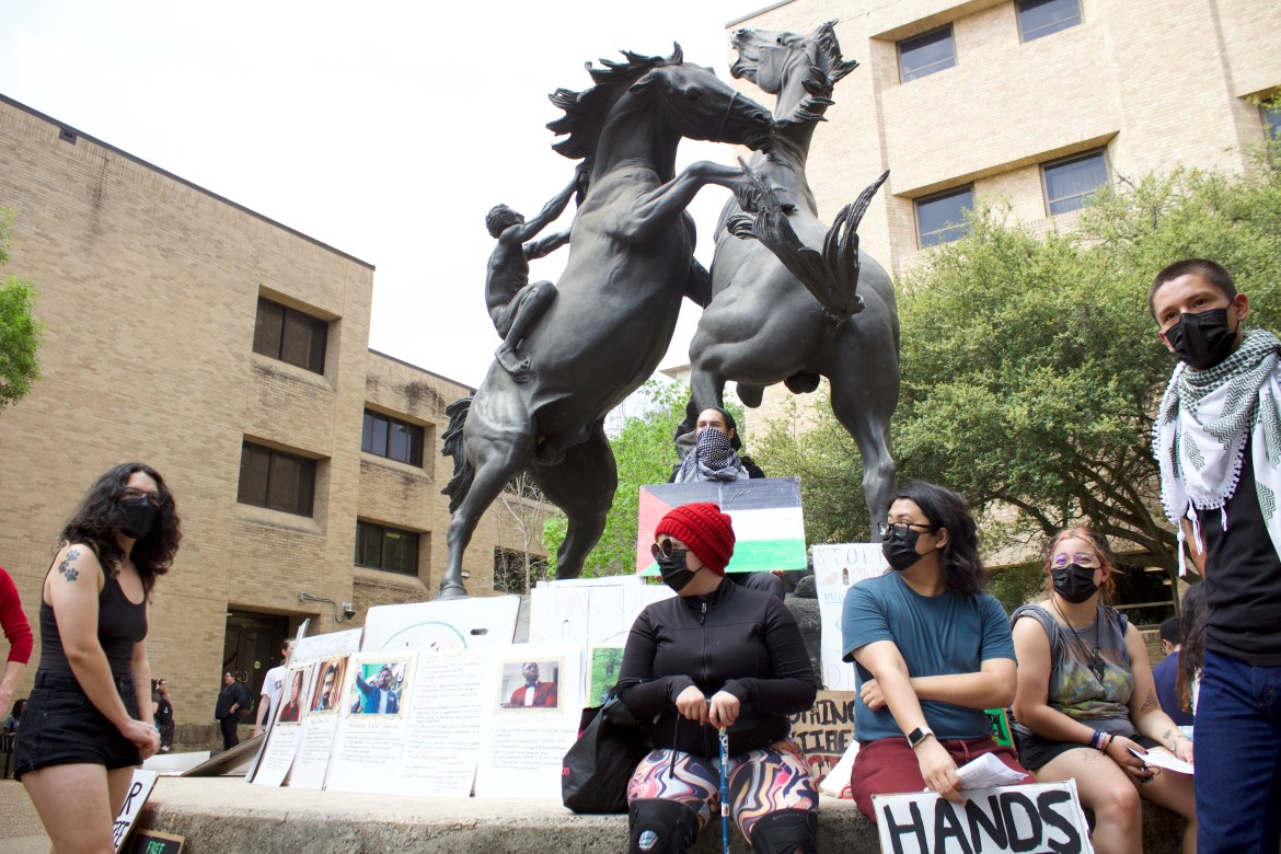 Student demonstrators sit on the base of a Stallion statue with a display of photos