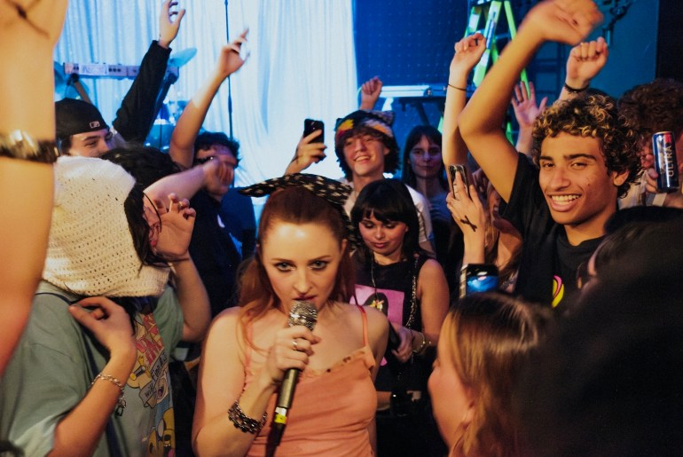 Mid shot from the crowd of Neggy Gemmy through the crowd looking directly at the camera while performing a song.