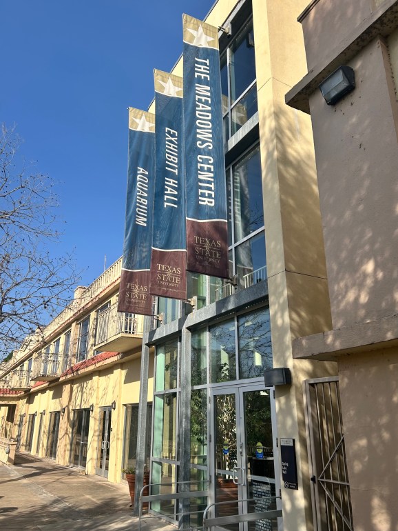Spring Lake Hall entrance with three navy, maroon and gold banners stating 'The Meadows Center', 'Exhibit Hall' and 'Aquarium'.