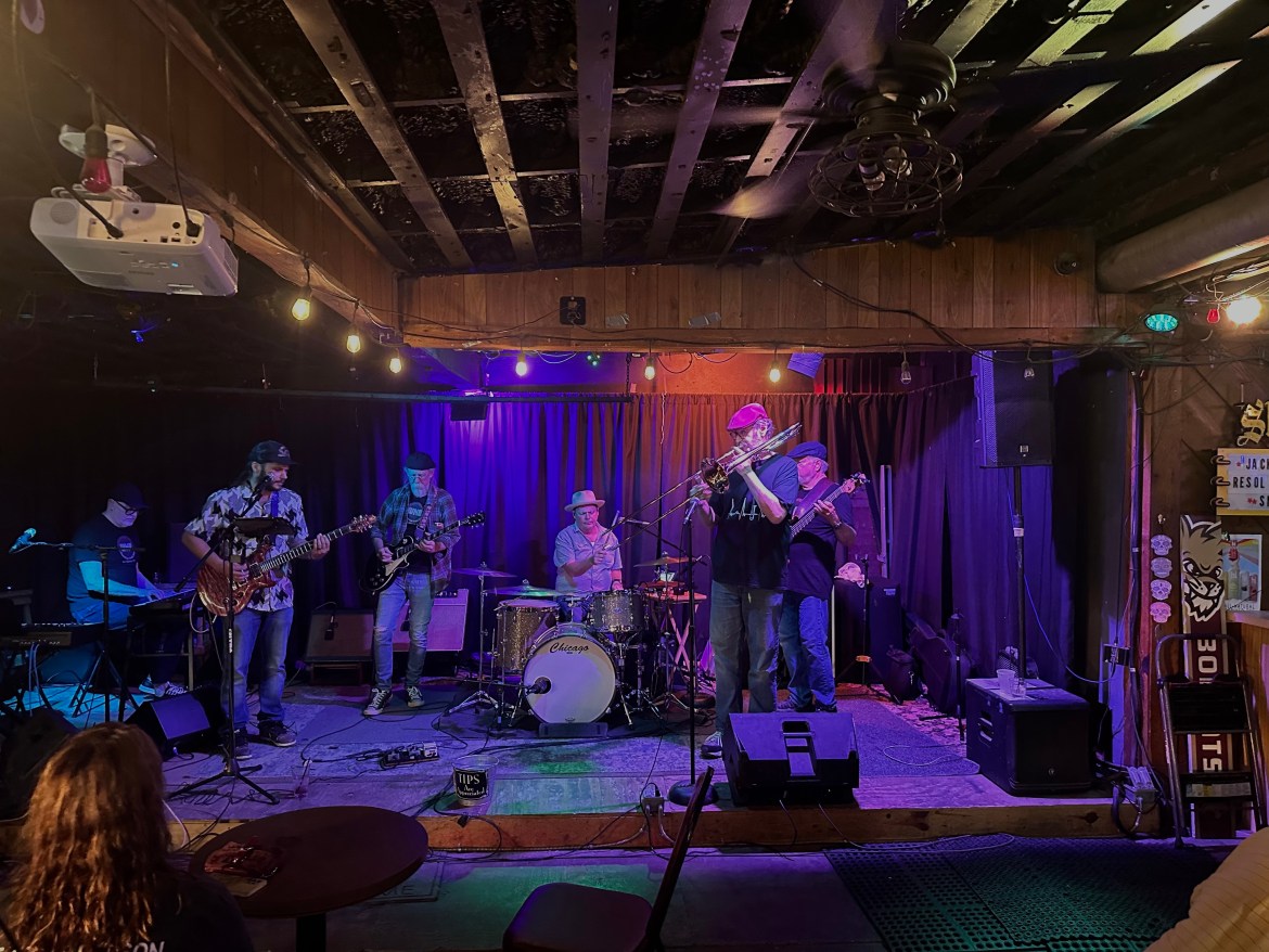 A band onstage playing instruments under purple lighting