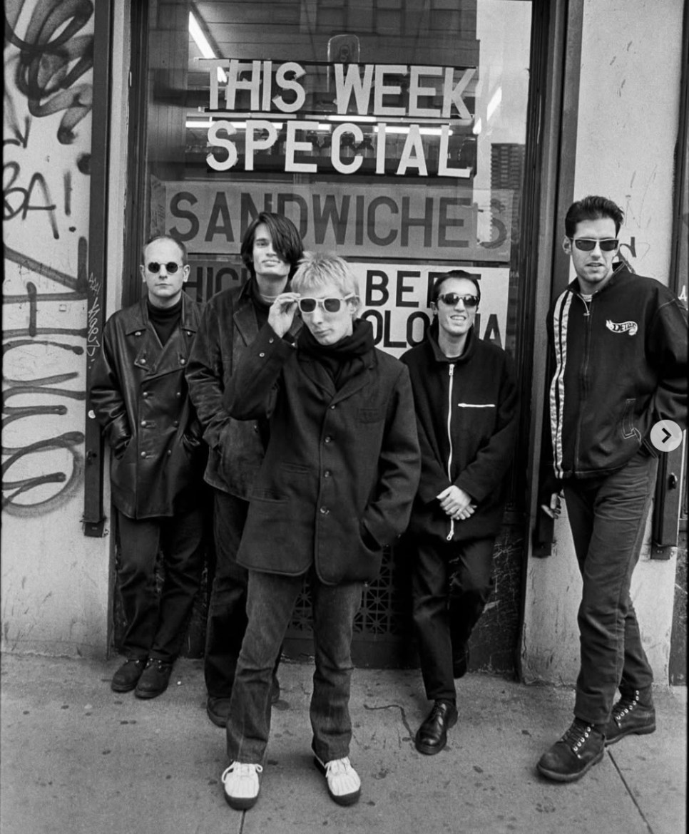 All five members of Radiohead pictured in black and white, posted in front of a sign that reads, “THIS WEEK SPECIAL” and underneath “SANDWHICHES”