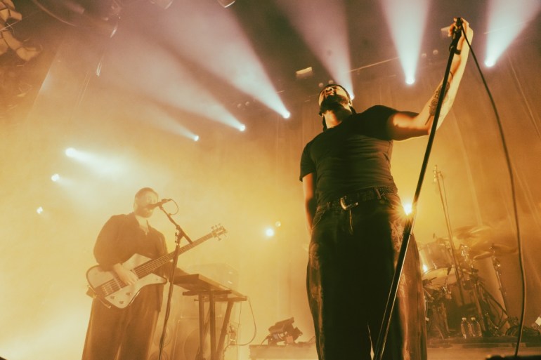 two men sharing the stage as they are showered in lights 