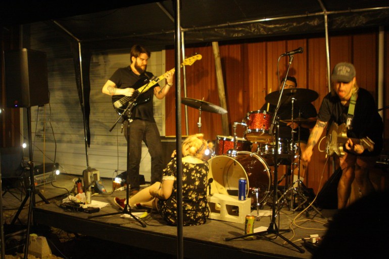 Band is playing while vocalist provides a powerful stage presence by sitting on the ground while singing.