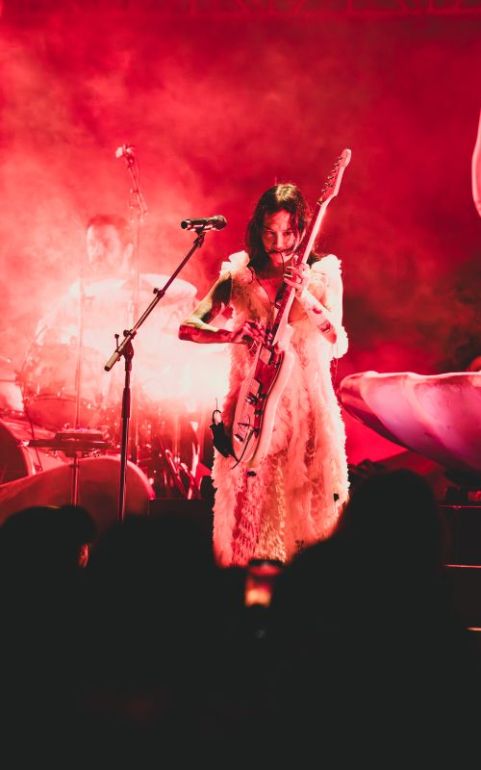 Michelle Zauner of Japanese Breakfast performs on stage, bathed in red light and smoke while playing a guitar.