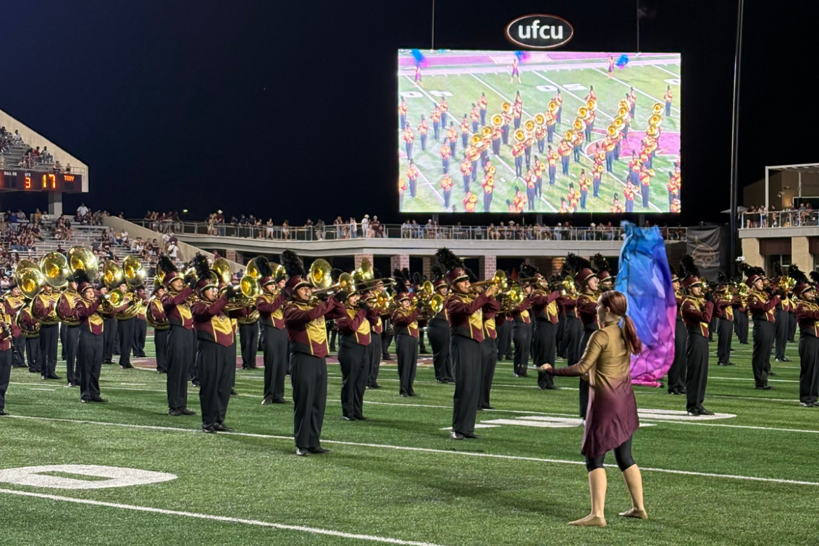 Marching band on a football field with a girl holding a flag.
