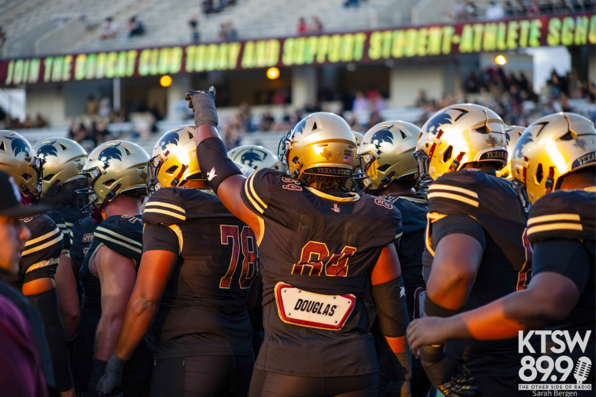 A group of Texas State offensive linemen in matching black uniforms huddle up before the start of the game.