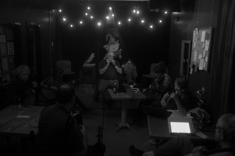 Musicians of Irish session in the backroom, in a circle around the room, playing different instruments.