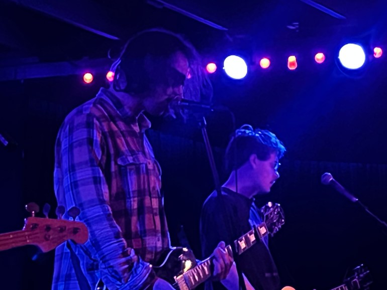 Two men play music while one sings up close to the mic