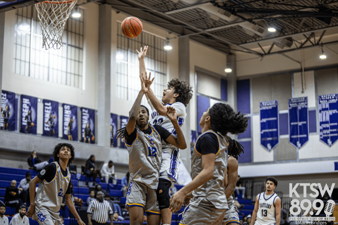 San Marcos player wearing a white jersey shoots the ball while trying to get around defender for the basket.