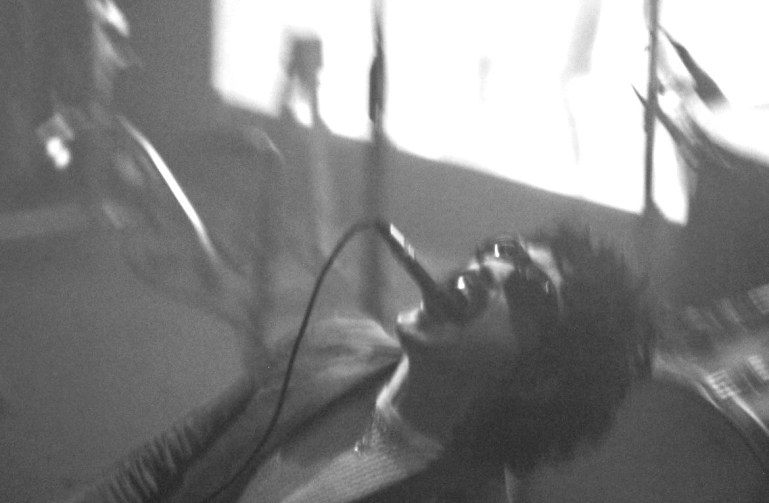vocalist and producer Stefan Baraza kneels back on the stage as he has a mic in his mouth hands free.