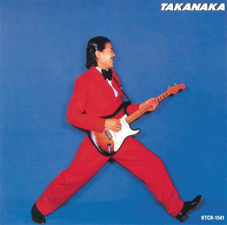 Masayoshi Takanka jumping in the air in a red suit with guitar in hand. 
