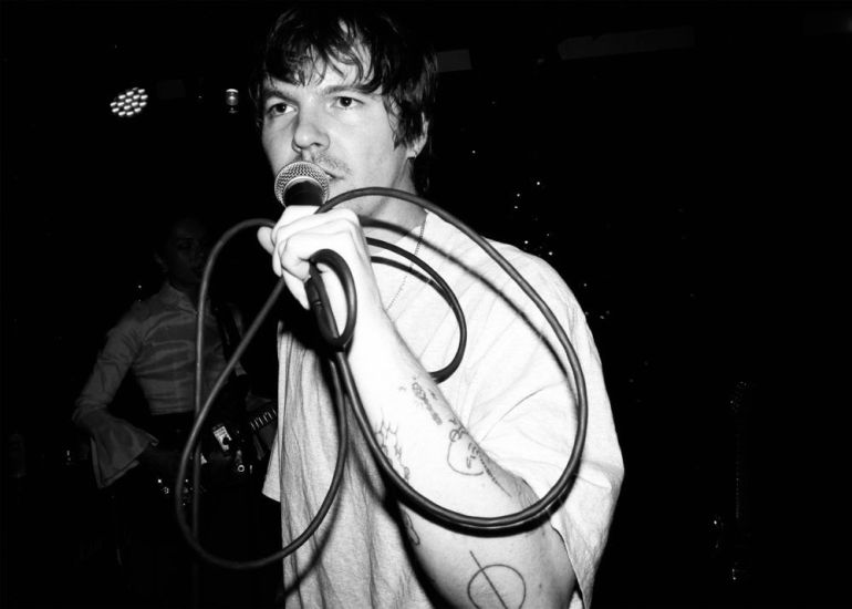 Shane Lavers holding a microphone, looking off into the distance in a dimly lit showroom 
