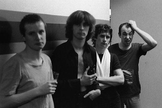 Black and white photograph of XTC lined up against a wall, backstage at the venue The Edge in Toronto, Canada. 