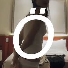 Large O with umlaut in front of a woman turned sideways in front of a hotel bed