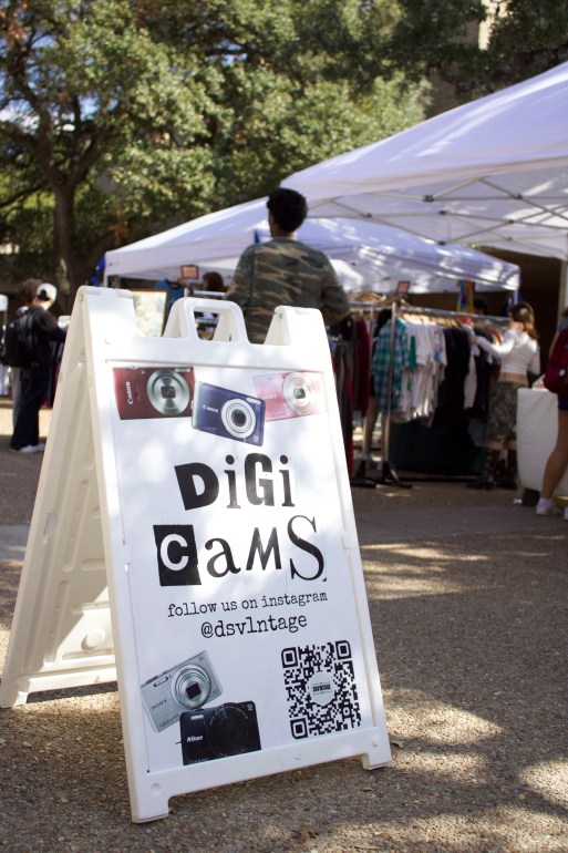 A sign for digital cameras sold at a DSV1NTAGE tent is displayed at an outdoor market. 
