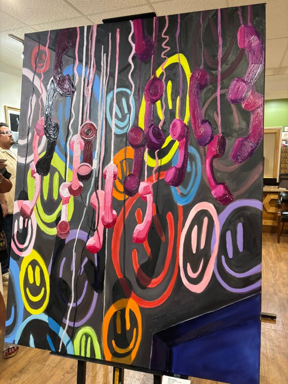 A vibrant and colorful painting of wired telephones hanging with smiley faces in the background.