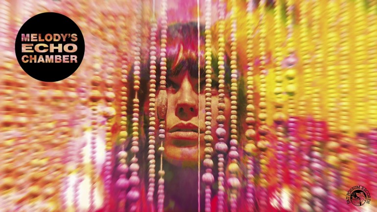 Close-up of a woman’s face behind hanging beads with vivid pink, orange, and yellow psychedelic colors.