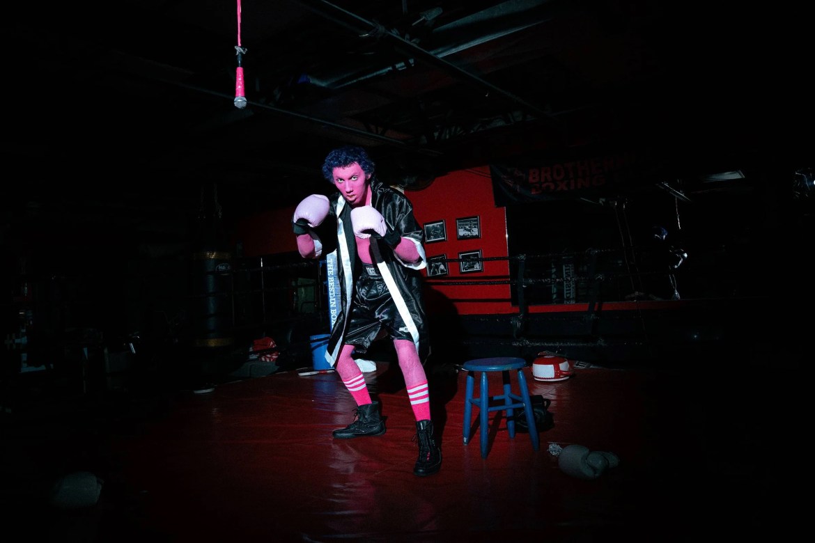 Perry Maysun getting ready for his show at the CenterStage Venue in Atlanta, GA. He’s dressed in wrestling attire with his full body painted pink. He’s posing in a boxing ring.