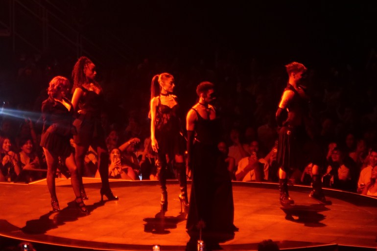 Ariana Grande and four dancers perform under intense red lighting on a circular part of the stage.