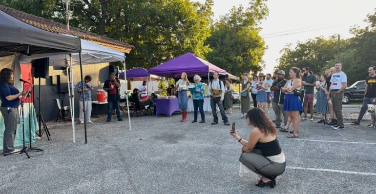 A speaker stands off to the side of a crowd behind Triple Six Social.