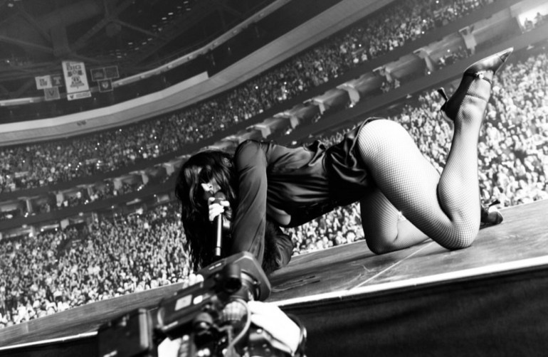 the image depicts singer Charlie xcx crawling onstage during a showing of her Music, Fashion, Film tour