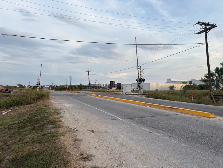 The rail crossing portion of Centerpoint Road in the evening. The crossing gate is raised while a warehouse is pictured in the background.