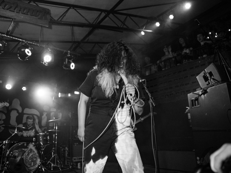 Black and white photo of Zayna of Sweet Pill screaming into a microphone on stage at Mohawk in Austin, Texas with the drummer of Sweet Pill behind her.