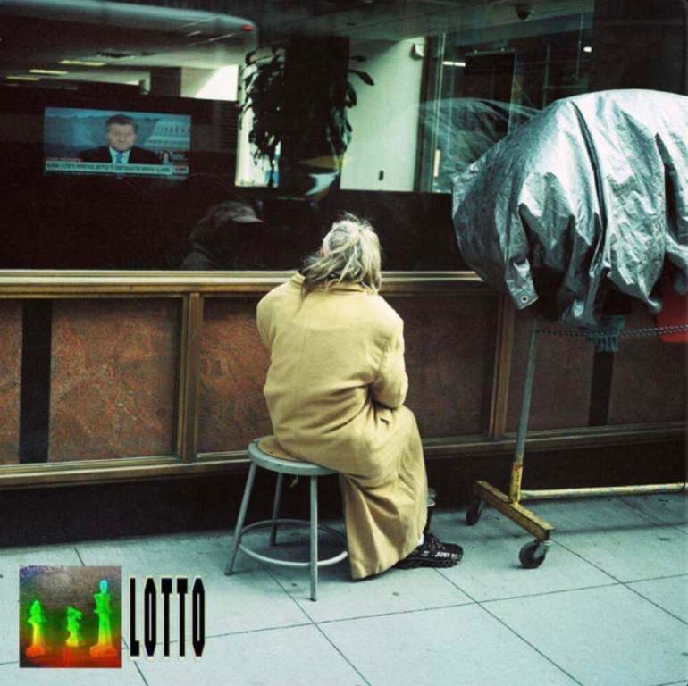 The image shows the backside of a woman in a long yellow dress sitting on a stool cross-legged and looking out a window that has a TV reflection. There’s a tarp on a rack on the right side and the words “LOTTO” are in bold in black in the bottom left corner with a small photo of three colorful human figurines.