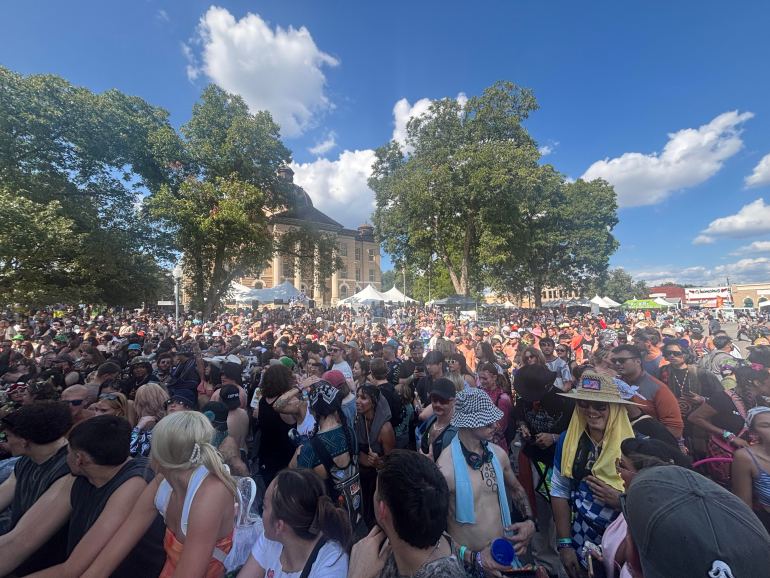 The image depicts the crowd that formed on the main stage at San Marcos block party. Tons of people are gathered together with the City Hall in the background. 