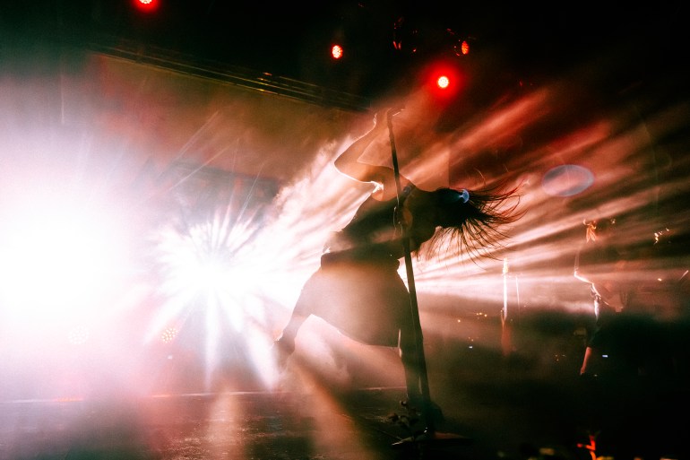 The lead singer of the band Molchat Doma is shown infront of a bright strobe light only showing his silhouette as he moves with the music and as his hair flies around.
