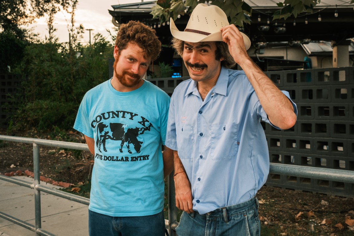 Musicians Dana and Alden are standing outside a venue, Alden is tipping his cowboy hat