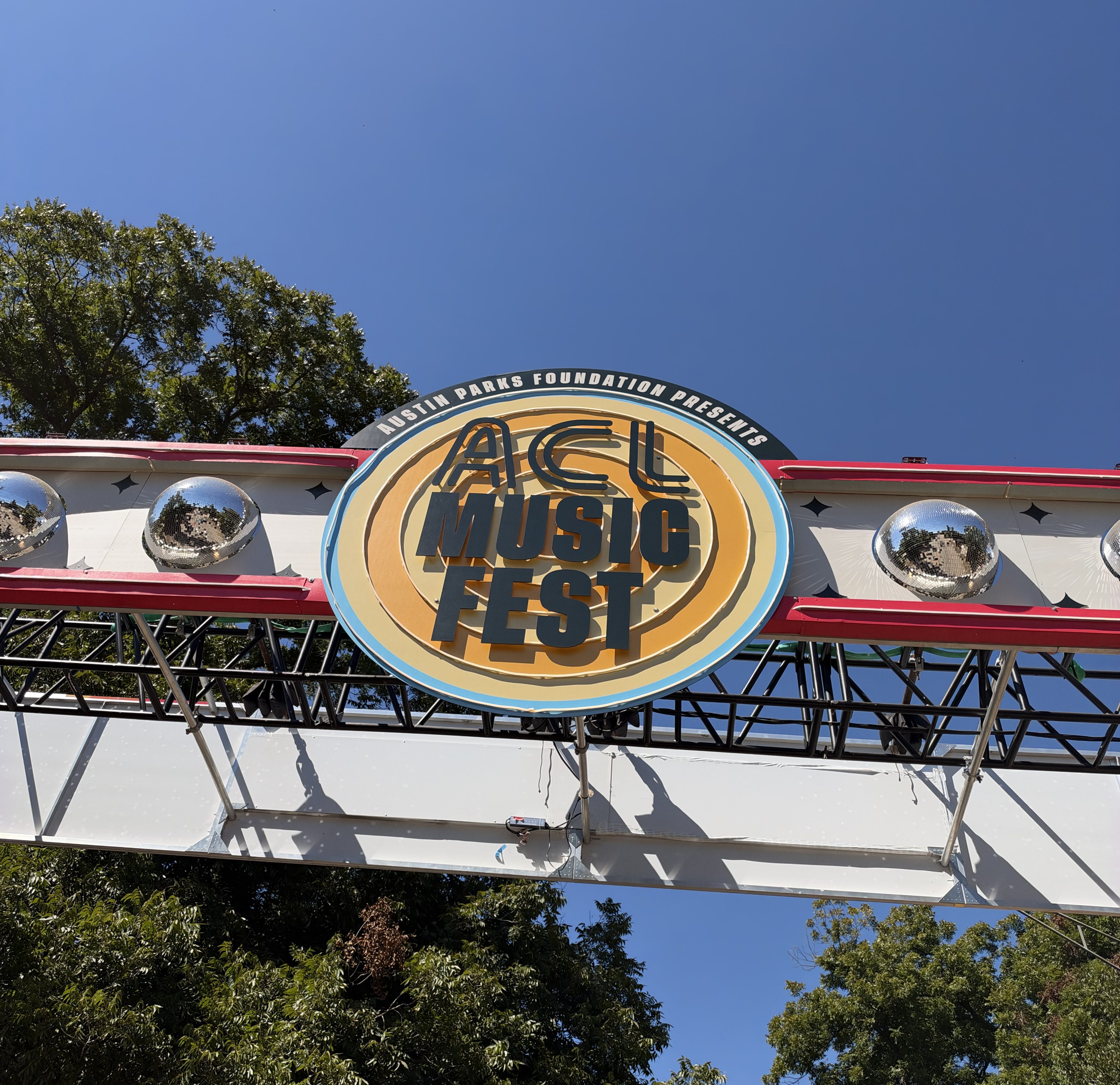 The image features the entrance gate to Austin City Limit music festival, with a sign saying "ACL" alongiside disco balls