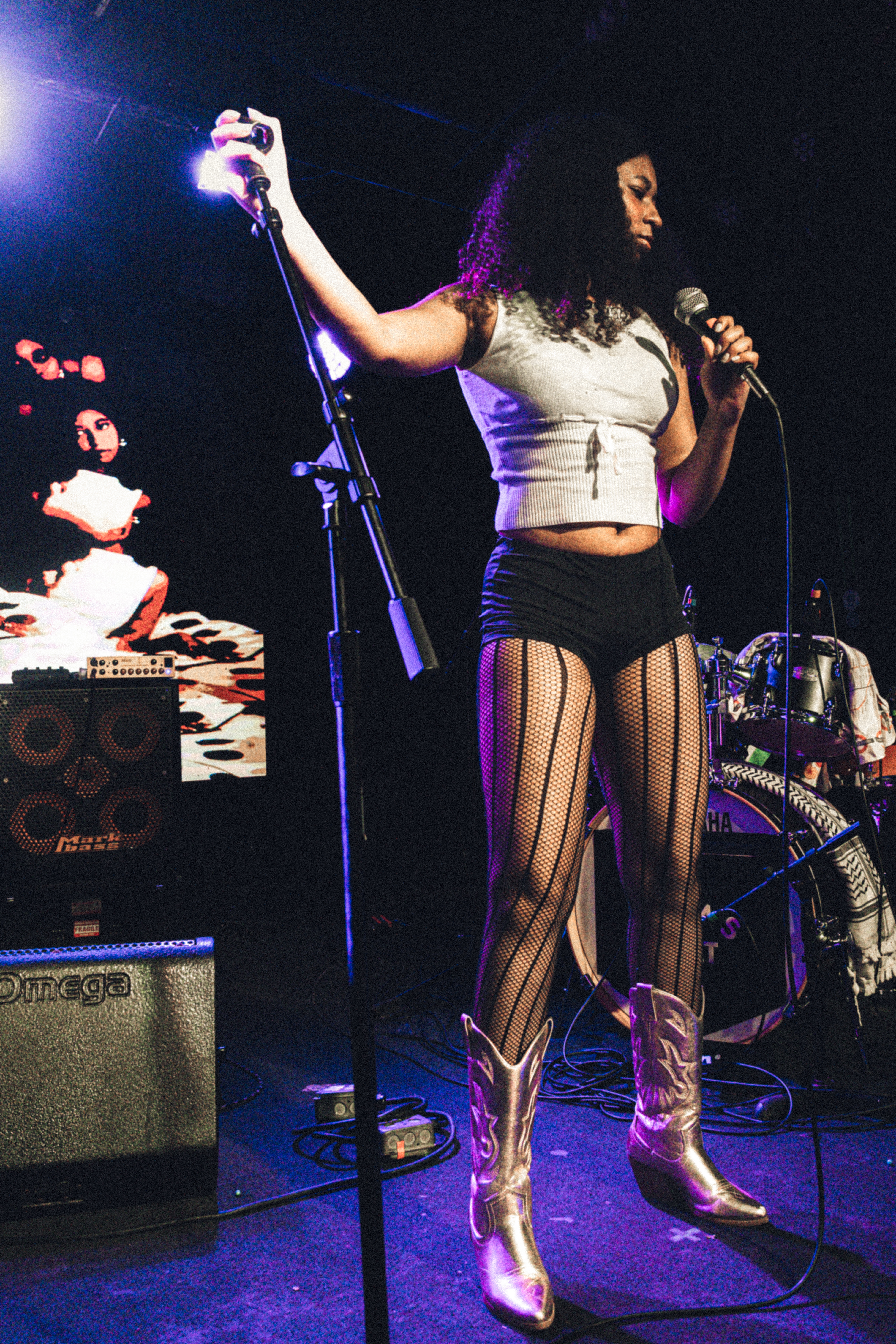 Singer Ania Hoo standing in front of her mic wearing a white knit tank and performing 