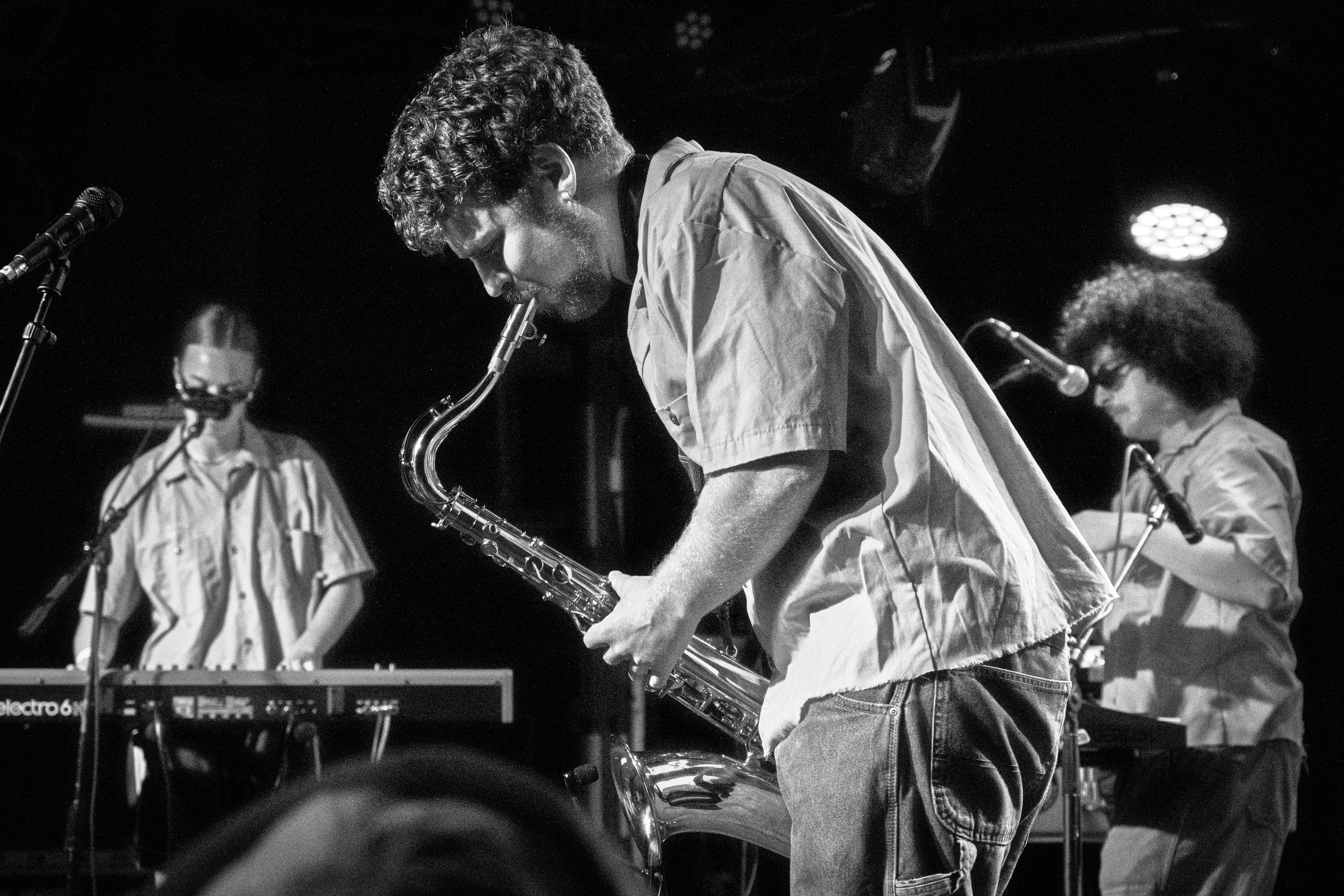 Black and White image depicts Dana playing saxophone, Ebba on keyboard, and Sam on synthesizer